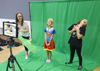 Kinder stehen auf einem Grünem Leintuch vor dem ipad und drehen einen Film