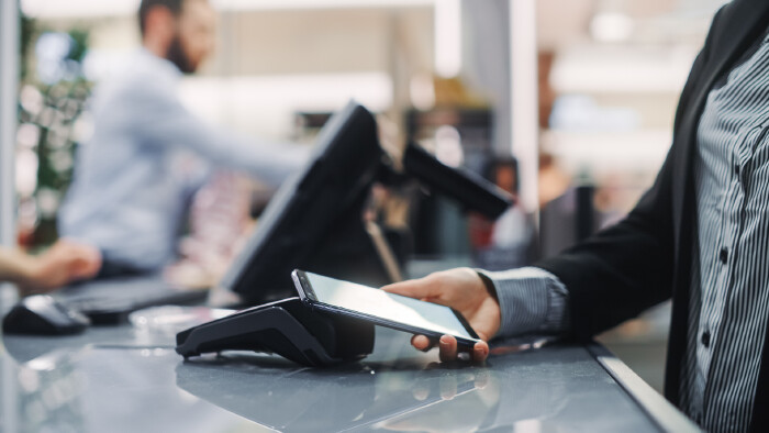Person bezahlt mit Smartphone kontaktlos an einem Bezahlterminal an einer Kasse.