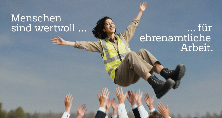 Eine grinsende ehrenamtlich engagierte Frau wird von einer Gruppe von Menschen in die Luft geworfen. Dabei steht der Text "Menschen sind wertvoll f&uuml;r ehrenamtliche Arbeit."