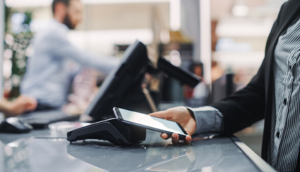 Person bezahlt mit Smartphone kontaktlos an einem Bezahlterminal an einer Kasse.
