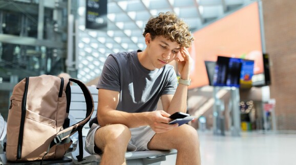 Junger Mann mit Rucksack sitzt am Flughafen