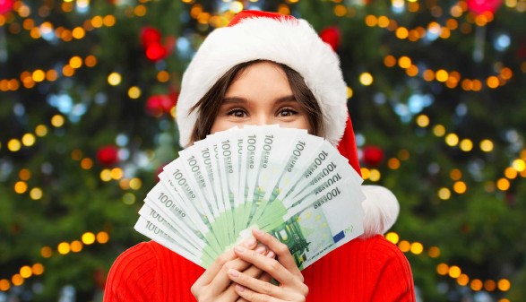 Frau mit Weihnachtsmütze hält Geldscheine vor ihr Gesicht. © Syda Productions, Adobe Stock