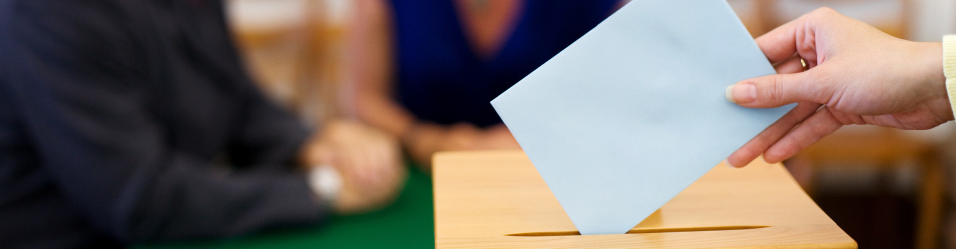 Vor unscharfem Hintergrund sieht man die Hand einer Frau, die ein Kurvert in eine Wahlurne steckt. © Gina Sanders, stock.adobe.com