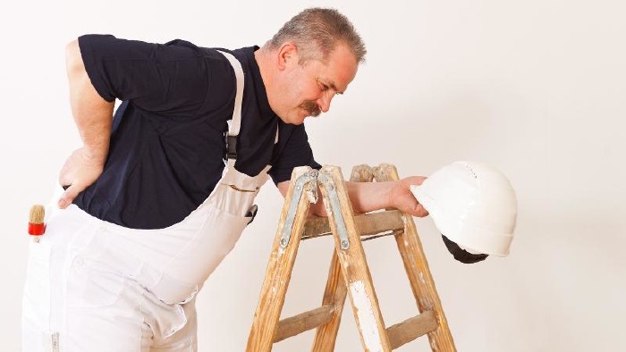 Maler mit Rückenschmerzen steht neben einer Leiter