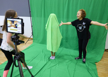 Ein Kind mit Grünem Tuch über dem Körper drehen einen Film vor der grünen Leinwand