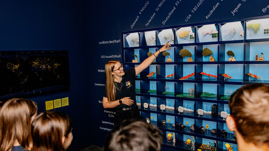 Kinder schauen auf eine Frau, die etwas am Energieregal erkl&auml;rt 