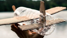 Kinderflugzeug aus einer PVC Flasche und Kartonfl&uuml;geln gebastelt segelt &uuml;ber einen See